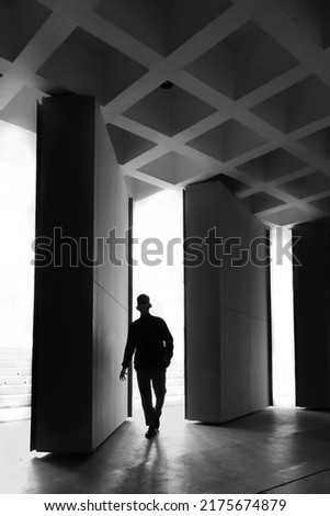 Silhouette of man walking through door on white light background. Black and white photography concept