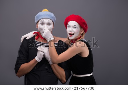 Waist-up portrait of funny mime couple looking at the camera, male mime holding his hands on the chest, female mime touching his nose isolated on grey background with copy place
