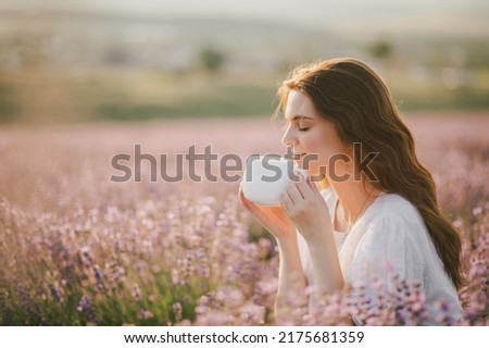 Young beautiful woman in white dress drinking healthy herbal tea in lavender field. Royalty-Free Stock Photo #2175681359
