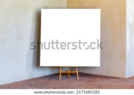 White blank picture mock up on wooden easel in old art gallery. Wooden easel with mock up empty blank canvas stand in vintage wall room , creative art concept. Empty template. Royalty-Free Stock Photo #2175685281