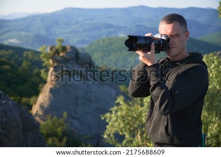 Nature photographer with digital camera on top of the mountain in the morning, taking photo of sunset mountains. Concept of travel lifestyle.