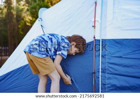 cute little caucasian boy helping to put up a tent. sunset shadows from trees. Family camping concept. High quality photo