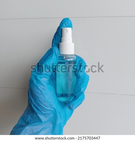 A blue gloved hand holds a bottle of alcohol spray