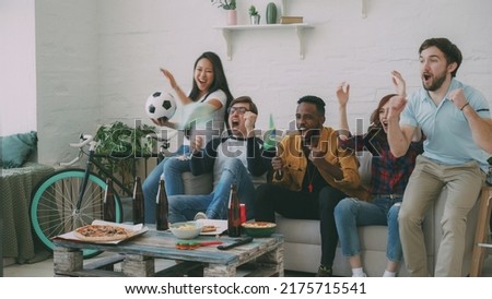 Multi-ethnic group of friends sports fans with Brazilian flags watching football championship on TV together at home indoors and cheering up favourite team Royalty-Free Stock Photo #2175715541