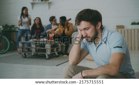 Young student guy feels upset and isolated while his friends celebrating party at home Royalty-Free Stock Photo #2175715551