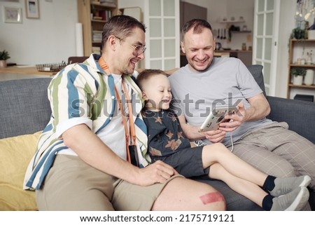 Gay couple watching funny video with son at home