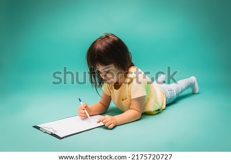 little girl draws on paper while sitting on an isolated background. child draws, space for text