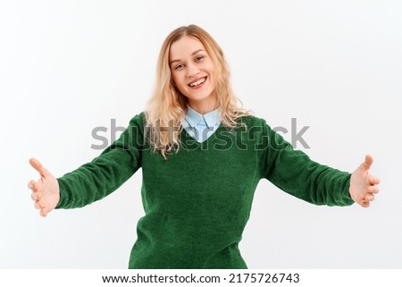Come into my arms. Portrait of friendly girl stretching hands and looking forward with happy smile to cuddle and welcome guests, wears casual clothes. Indoor studio shot on white background