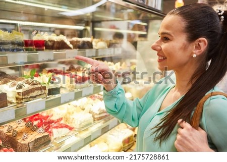 Smiling young female customer at the refrigerated shelf buying a cake in the pastry shop or bakery