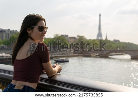 Young woman with sunglasses in the foreground with the Seine River and the Eiffel Tower in the background on a sunny day.