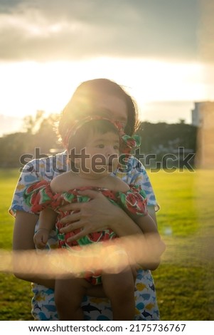 Silhouette photo of a lovely couple of mother and infant baby are enjoy playing at the outdoor park, with colorful blue sky as background. Photo contained noise due to lowlight condition.