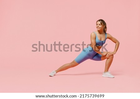 Full size young sporty athletic fitness trainer woman wears blue tracksuit spend time in home gym train do stretch legs squat exercise isolated on pastel plain pink background. Workout sport concept