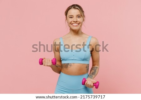 Young fun strong sporty athletic fitness trainer instructor woman wear blue tracksuit spend time in home gym hold female dumbbells isolated on pastel plain light pink background. Workout sport concept