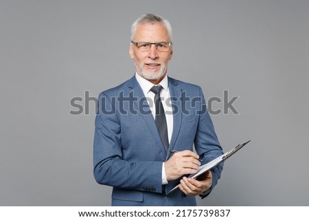 Confident elderly gray-haired bearded business man in blue suit shirt tie isolated on grey background studio portrait. Achievement career wealth business concept. Hold clipboard with papers document Royalty-Free Stock Photo #2175739837