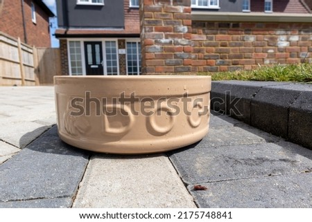 Brown ceramic dog water bowl on a house driveway for the use of passing dogs