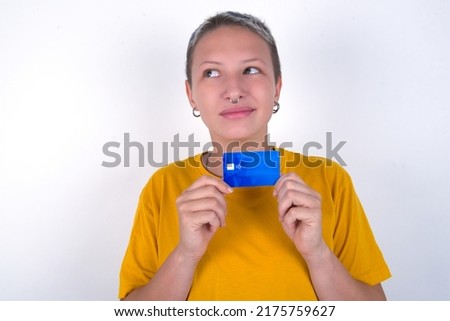Photo of cheerful Caucasian woman with short hair wearing yellow T-shirt over white wall hold debit card look empty space
