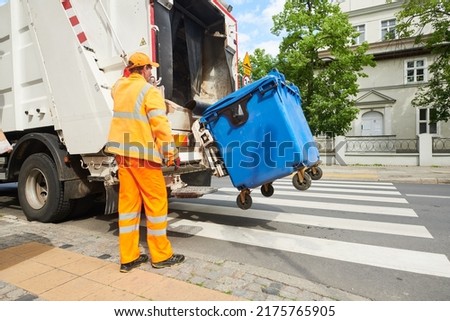 garbage and waste removal services. Worker loading waste bin into truck at city Royalty-Free Stock Photo #2175765905
