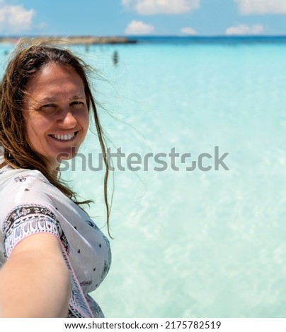 Close up portrait of a smiling woman who takes selfie image on a beautiful beach.The picture invites friends or other people, tourists to join her on a beautiful beach or on vacation.Summer vacation. 