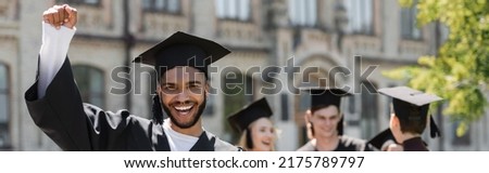 Excited african american bachelor in cap showing yes gesture in park, banner Royalty-Free Stock Photo #2175789797