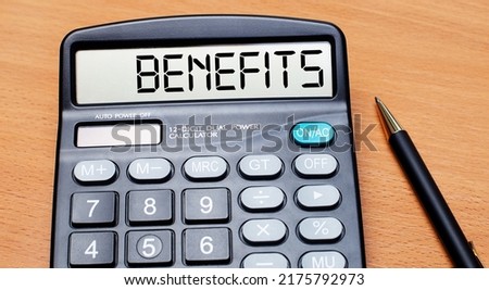 On a wooden table there is a black pen and a calculator with the text BENEFITS. Business concept