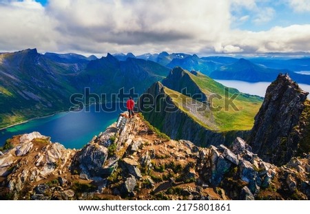 Hiker standing on the top of Husfjellet Mountain on Senja Island in northern Norway and enjoying spectacular views over surrounding fjords and mountains. Royalty-Free Stock Photo #2175801861