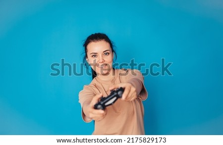 A cheerful girl in a beige T-shirt, isolated on a blue background, studio portrait. Lifestyle concept. Layout of the copy space. Play the game with the joystick.