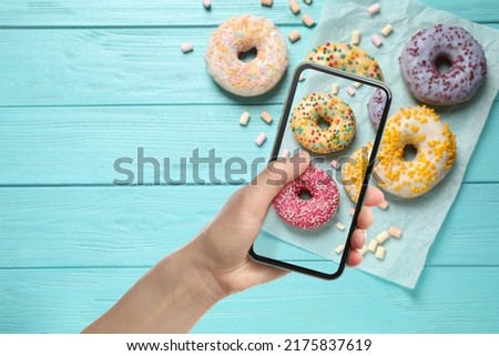 Woman taking picture of tasty donuts on light blue wooden table, top view