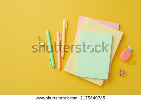 School supplies concept. Top view photo of colorful stationery stack of diaries pineapple shaped eraser binder clips and pens on isolated yellow background