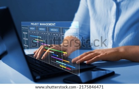 Project manager working on laptop and updating tasks and milestones progress planning with Gantt chart scheduling interface for company on virtual screen.  Business Project Management System.  Royalty-Free Stock Photo #2175846471