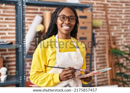 African american woman artist smiling confident holding paintbrush and palette at art studio Royalty-Free Stock Photo #2175857457