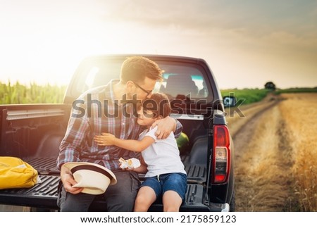 father and son sits on trunk of truck in wheat field. father hugs and kisses his son Royalty-Free Stock Photo #2175859123