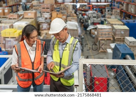 Male inventory supervisor explaining work plan in his notebook with young female worker at industry factory warehouse