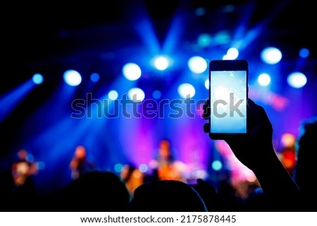 Hand with a smartphone records live music festival and taking photo of concert stage