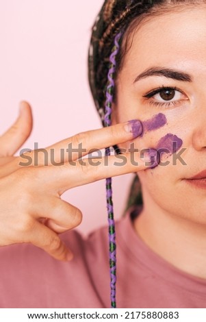 Girl paints half of her face with purple paint.
