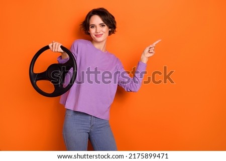 Portrait of pretty positive girl hold wheel direct finger empty space offer isolated on orange color background