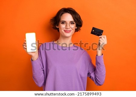 Photo of cute funny lady wear violet sweatshirt spectacles bank card showing modern device empty space isolated orange color background