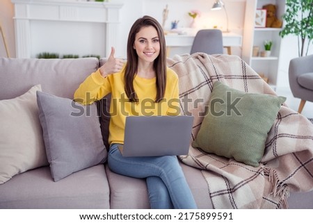 Portrait of attractive trendy cheerful girl using laptop showing thumbup ad rate offer web order at home apartment indoors