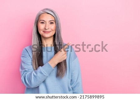 Photo of charming pretty retired woman blue sweater smiling pointing empty space isolated pink color background