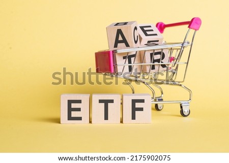 ETF - Exchange Traded Fund text on wooden cubes, on a light yellow table with mini shopping cart