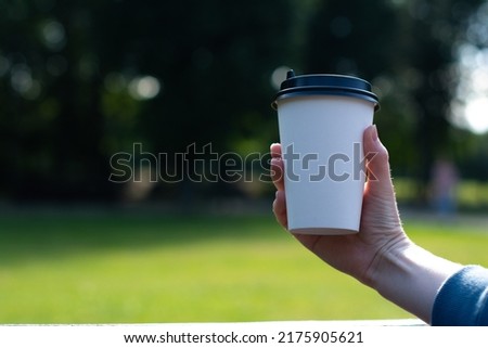 White paper cup of coffee in hand. For mock up. Isolated. On nature background