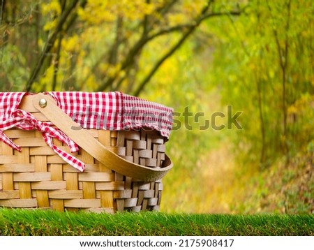 On a green lawn, a beautifully decorated straw picnic basket against the backdrop of a picturesque autumn nature. Recreation, relaxation, picnic, Thanksgiving, Harvest Day celebration.