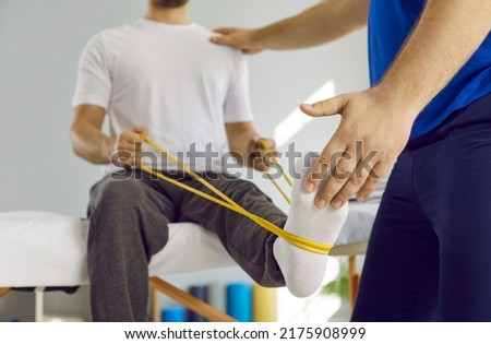 Male patient using elastic band while doing physical exercises for leg muscles at modern clinic, rehabilitation center or hospital. Close up of man's foot. Physiotherapy concept Royalty-Free Stock Photo #2175908999