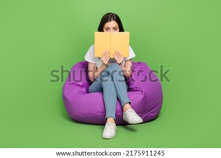 Photo of excited impressed woman dressed white t-shirt sitting bean bag interesting book cover face isolated green color background