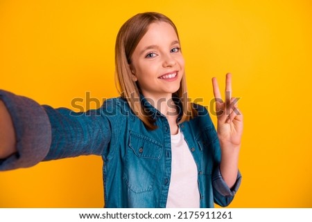 Portrait of cheerful funny cute girl make selfie hand fingers demonstrate v-sign isolated on yellow color background