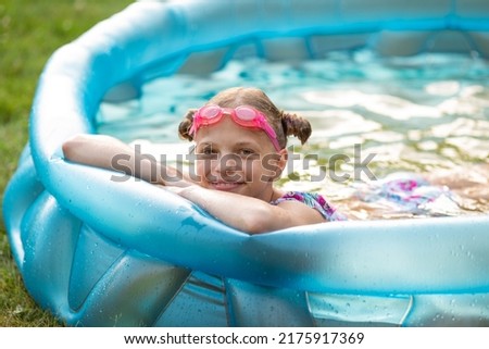 Teenage girl swims in a blue inflatable pool swims in a pool in the garden next to a house