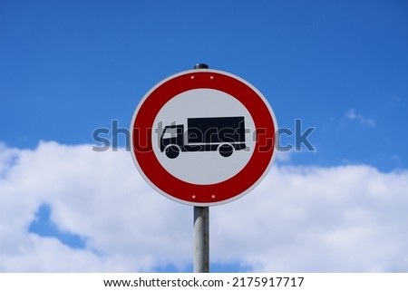 The sign means that entry for trucks is prohibited. Trucks are not allowed to use the road. A truck is visible on the sign. Sky and clouds in the background.                               