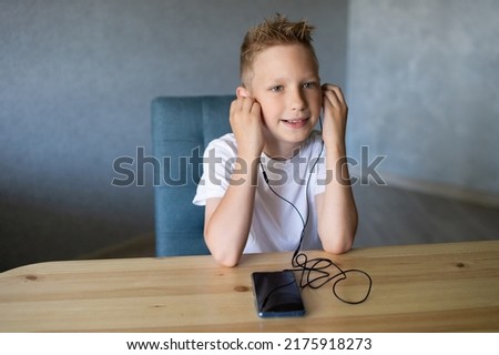 A cute boy has connected wired headphones to his phone and is listening to music