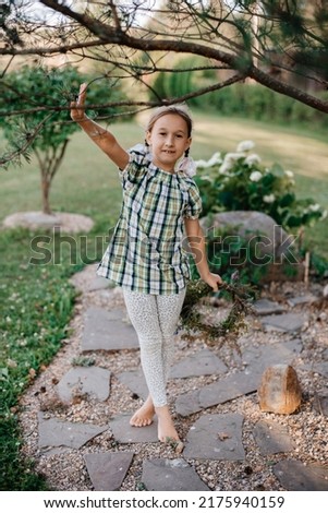 Little girl with wreath on her head makes yoga, she breathes and dance. Child sits on grass barefoot. She is lovely and peacefool. Concept of physical activity, child gymnastics, folk culture. 