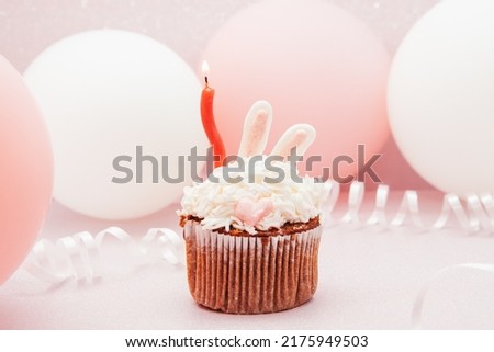 Bunny cupcake and red candle on glitter pink background with air balloons, happy birthday card