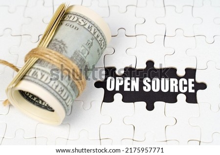 Business concept. Dollars lie on white puzzles, on a black surface there is an inscription - Open Source